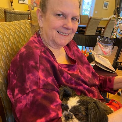 Resident smiling with a dog in a cozy common area