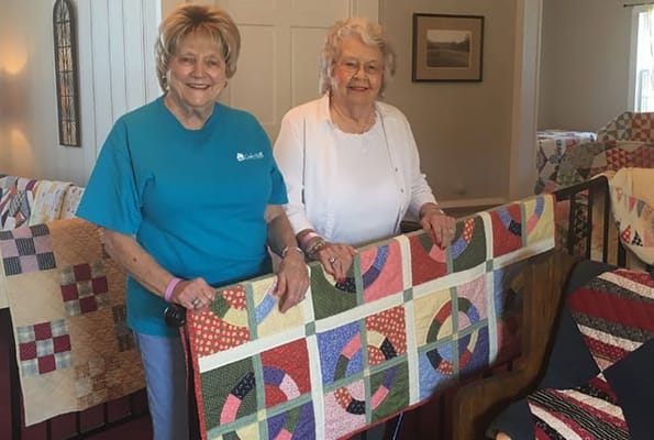 Residents showcasing handmade quilts in a common area