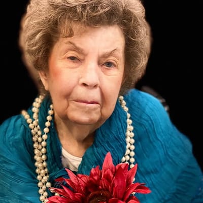 An elderly woman holding a flower and wearing a blue scarf