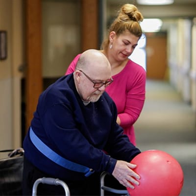 A caregiver assisting a resident with a ball in a hallway
