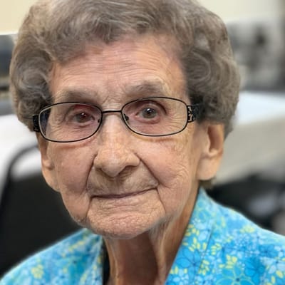 An elderly woman with glasses smiling at the camera
