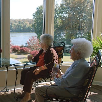 Two residents enjoying drinks by a large window overlooking a lake