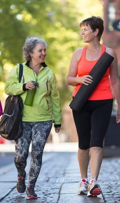 Two women walking outdoors with yoga mats