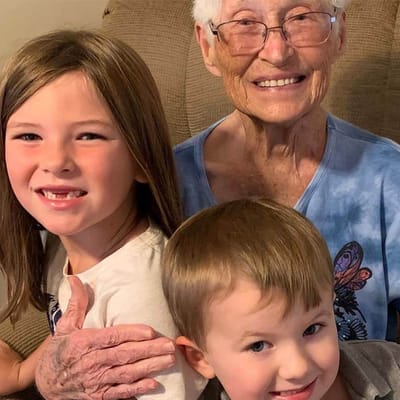 An elderly woman posing with two children, smiling