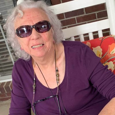 Elderly woman smiling on a porch with sunglasses