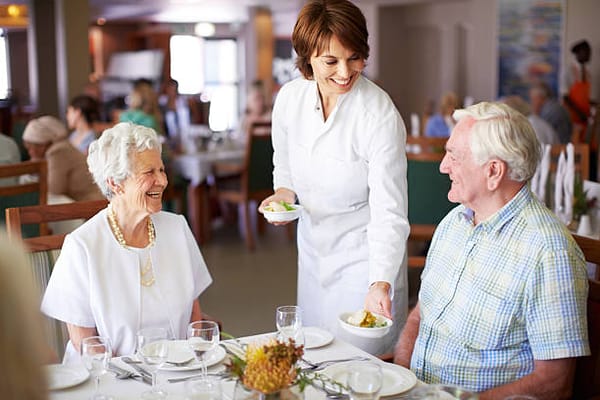 Server serving food to residents in a dining room