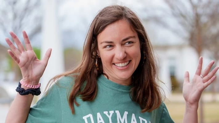 A staff member smiling and waving outdoors