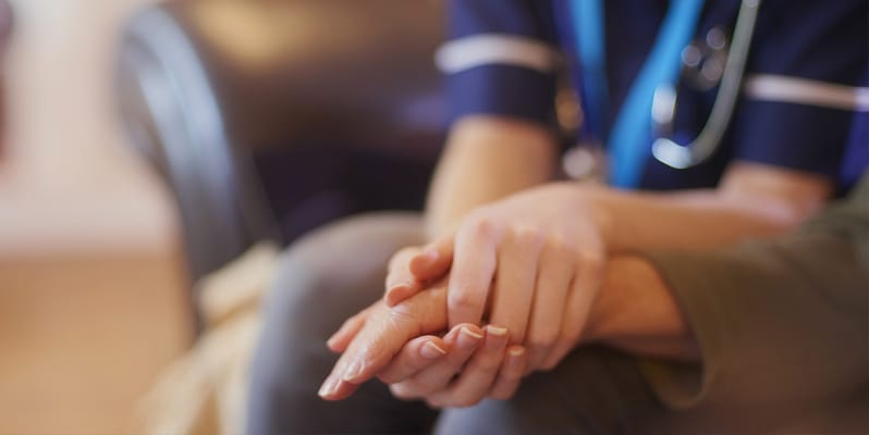 A caregiver holding a senior's hands in comfort