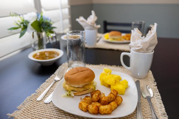 Plated meal featuring a sandwich, potatoes, and fruit