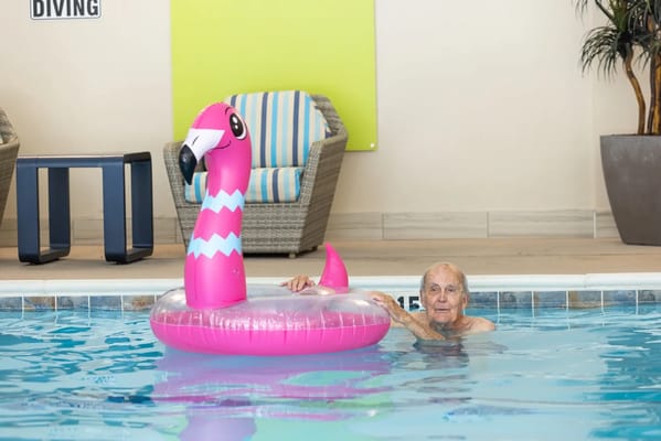 An elderly man in a pool with a flamingo float