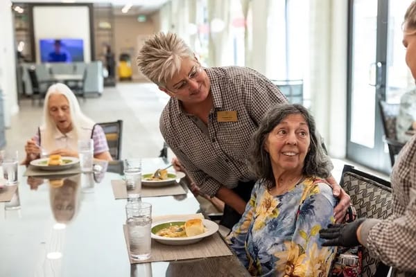 Residents enjoying a meal in the dining room with staff interaction