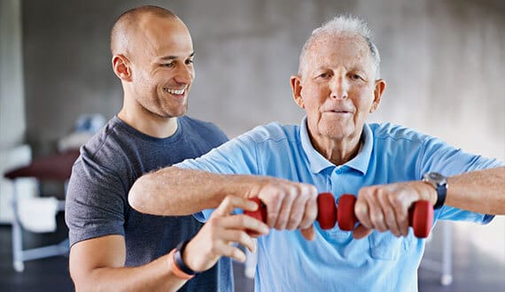 Older man exercising with weights, assisted by trainer