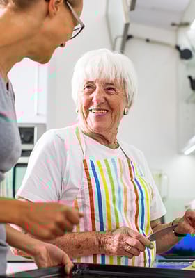 Senior resident cooking with staff member in the kitchen
