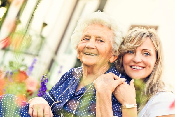 A smiling senior woman and caregiver in a garden