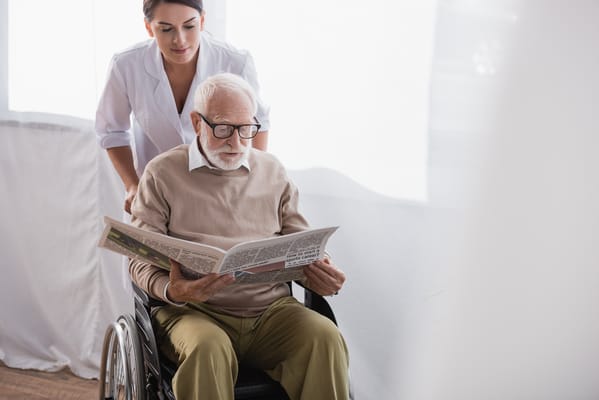 A senior man reading a newspaper with caregiver assistance