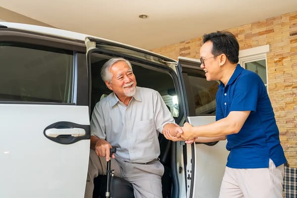 An elderly man smiling and shaking hands with a staff member by a vehicle