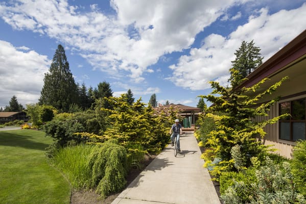 A resident biking on a garden pathway in a senior living facility