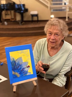 Resident enjoying painting activity with a glass of wine