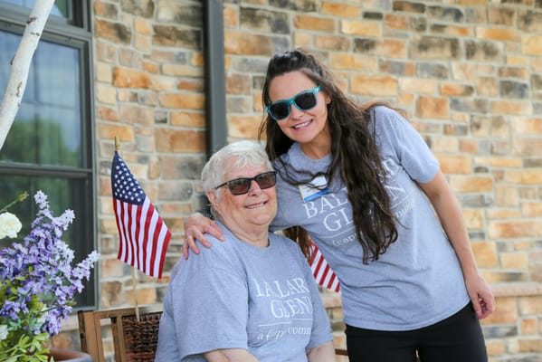 Resident and staff member smiling outdoors with American flags
