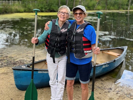 Two residents smiling by a canoe in a natural setting