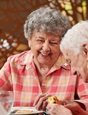 Two smiling elderly women enjoying a meal together
