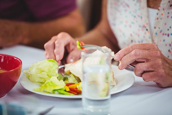 Hands holding a fork and knife with a plate of food