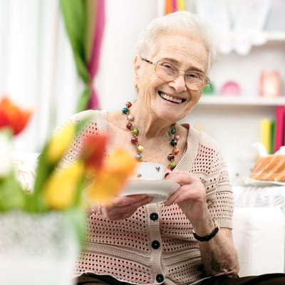 An elderly woman smiling while holding a teacup