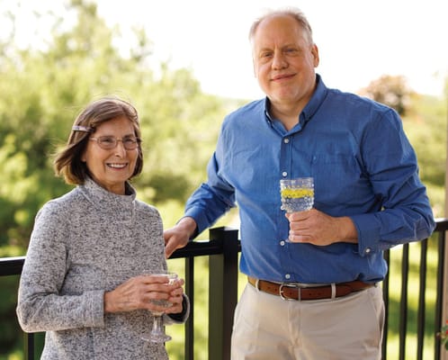 Residents enjoying drinks on a balcony with a green backdrop