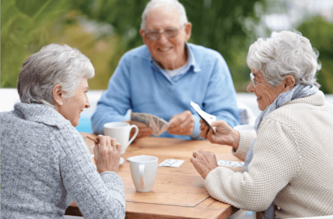 Seniors playing cards outdoors at a table
