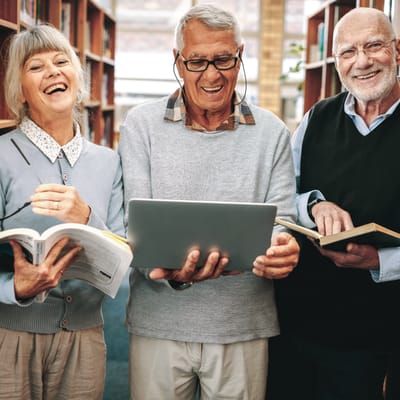 Three seniors engaging with a laptop in a library setting.