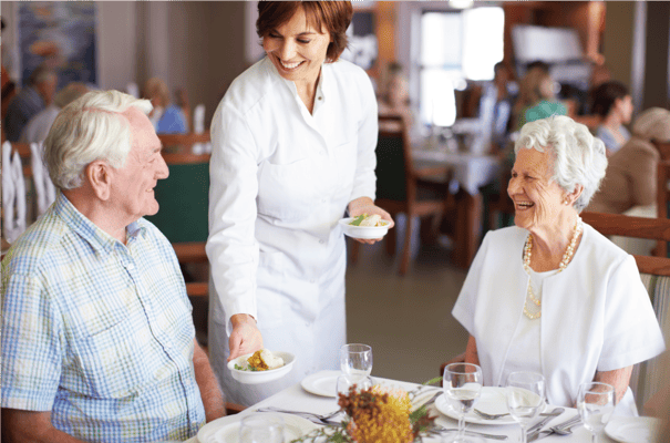 A staff member serving dessert to residents in the dining room