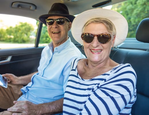 Two smiling seniors in a car with sunglasses