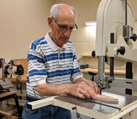 An elderly man using a bandsaw in a workshop