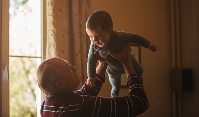 An elderly man joyfully playing with a baby indoors