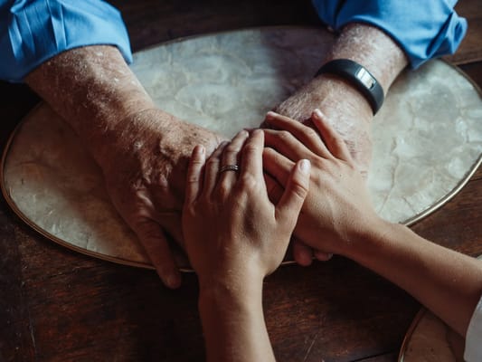Hands of a senior and a younger person clasped together