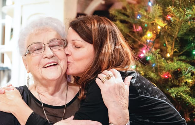 Resident and staff member sharing a warm embrace by a decorated Christmas tree