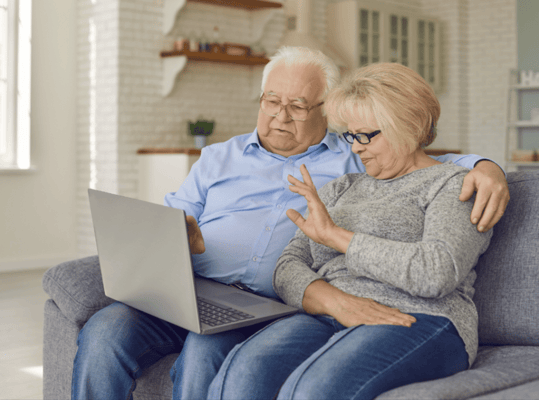 Two senior residents using a laptop together on a couch