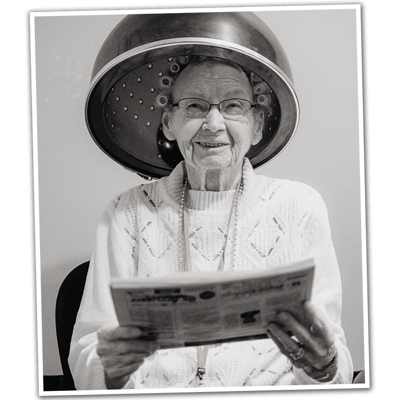 Elderly woman with a hair dryer reading a newspaper
