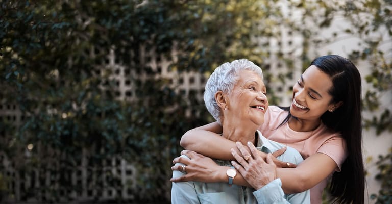 A caregiver embracing a senior woman outdoors