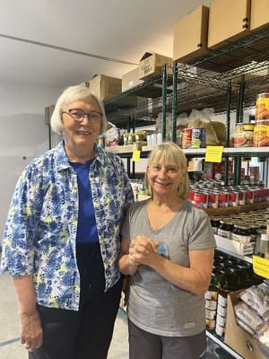 Two women smiling in a storage area with shelves