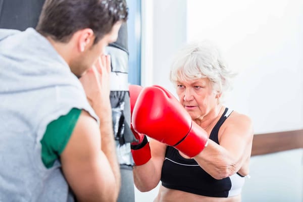 Senior woman boxing with a trainer indoors