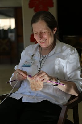 A staff member knitting and smiling in a common area