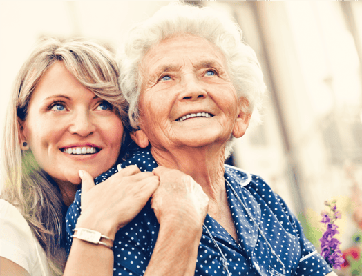 A senior woman smiling with a young woman outdoors