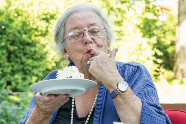 A smiling senior woman enjoying cake outdoors