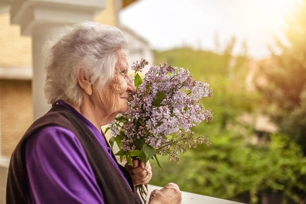 An elderly woman enjoying flowers on a balcony