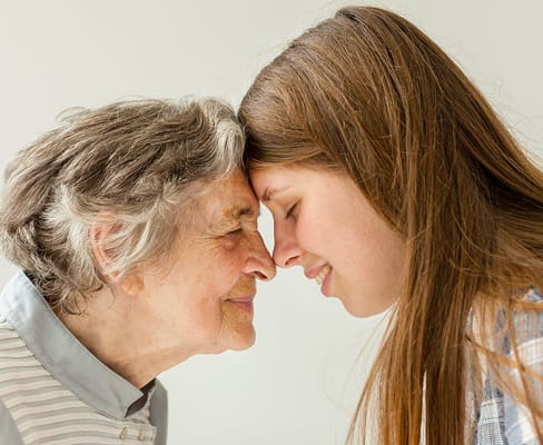 An elderly woman and a young girl smiling with foreheads touching