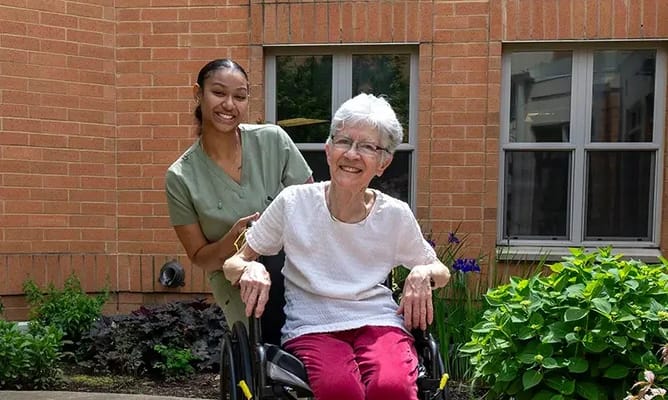 Resident and staff member smiling outside in a garden