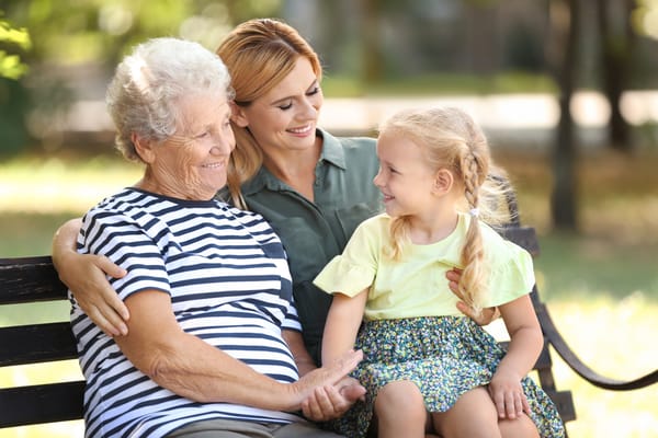 A senior resident with family outdoors on a bench