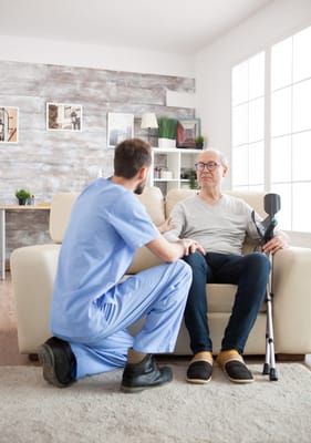 A caregiver assisting an older man in a cozy living room