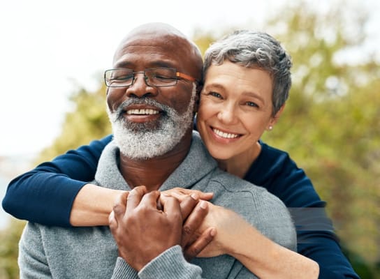Two smiling seniors embracing outdoors